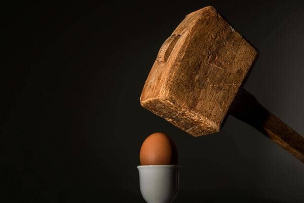 un maillet en bois prêt à écraser un oeuf dans un coquetier